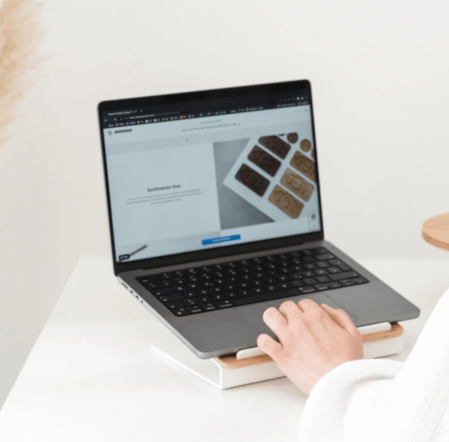 Person using a laptop placed on a Kansoki wooden laptop stand with white metal base on a desk.