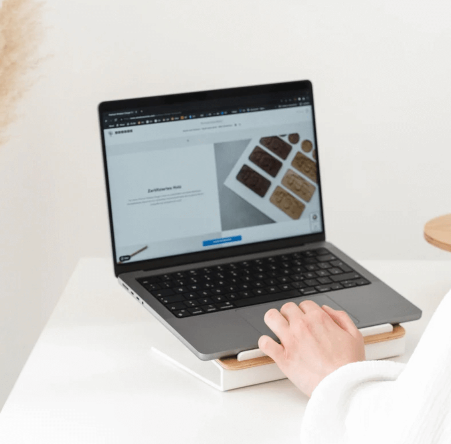 Person using a laptop placed on a Kansoki wooden laptop stand with white metal base on a desk.